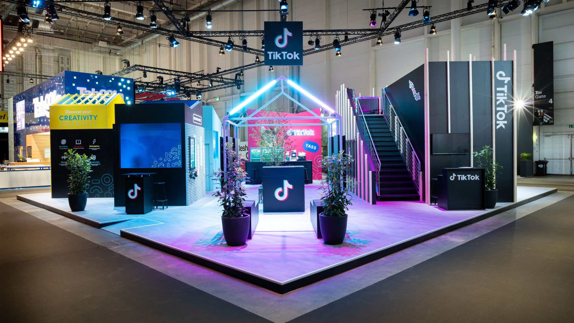 A colorful exhibition booth with a "Discover Music" section, tables with benches, and a vibrant TikTok area featuring neon lights and playful graphics. Battle Royal Studios