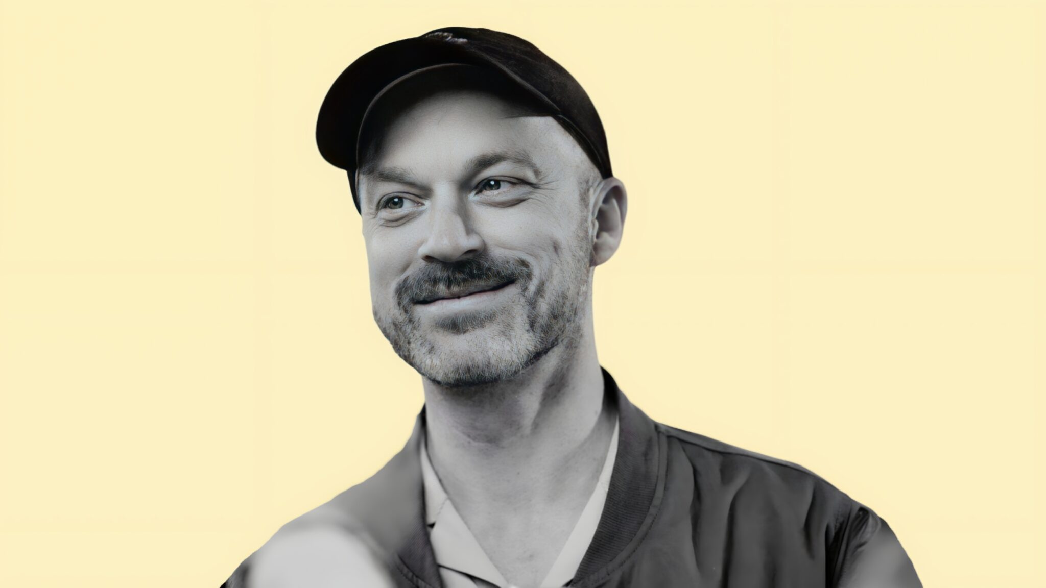 Black and white portrait of a smiling man in a cap on a pale yellow background