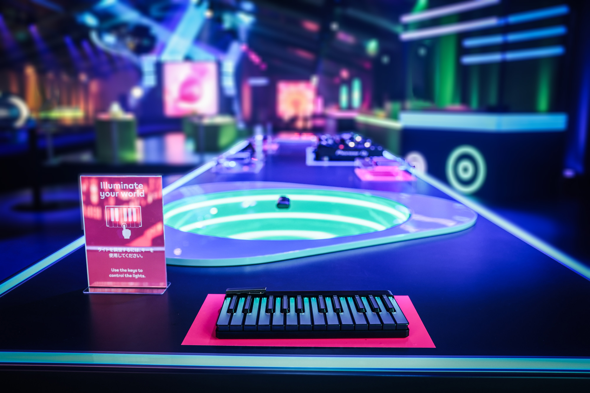 Empty neon-lit room with a glowing oval game table, a keyboard and a small sign in blue and pink light.