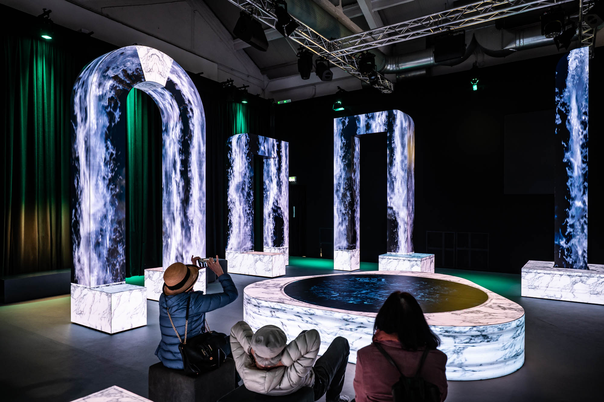 Guests sitting around a central fountain surrounded by LED arches showing flowing blue marble textures.