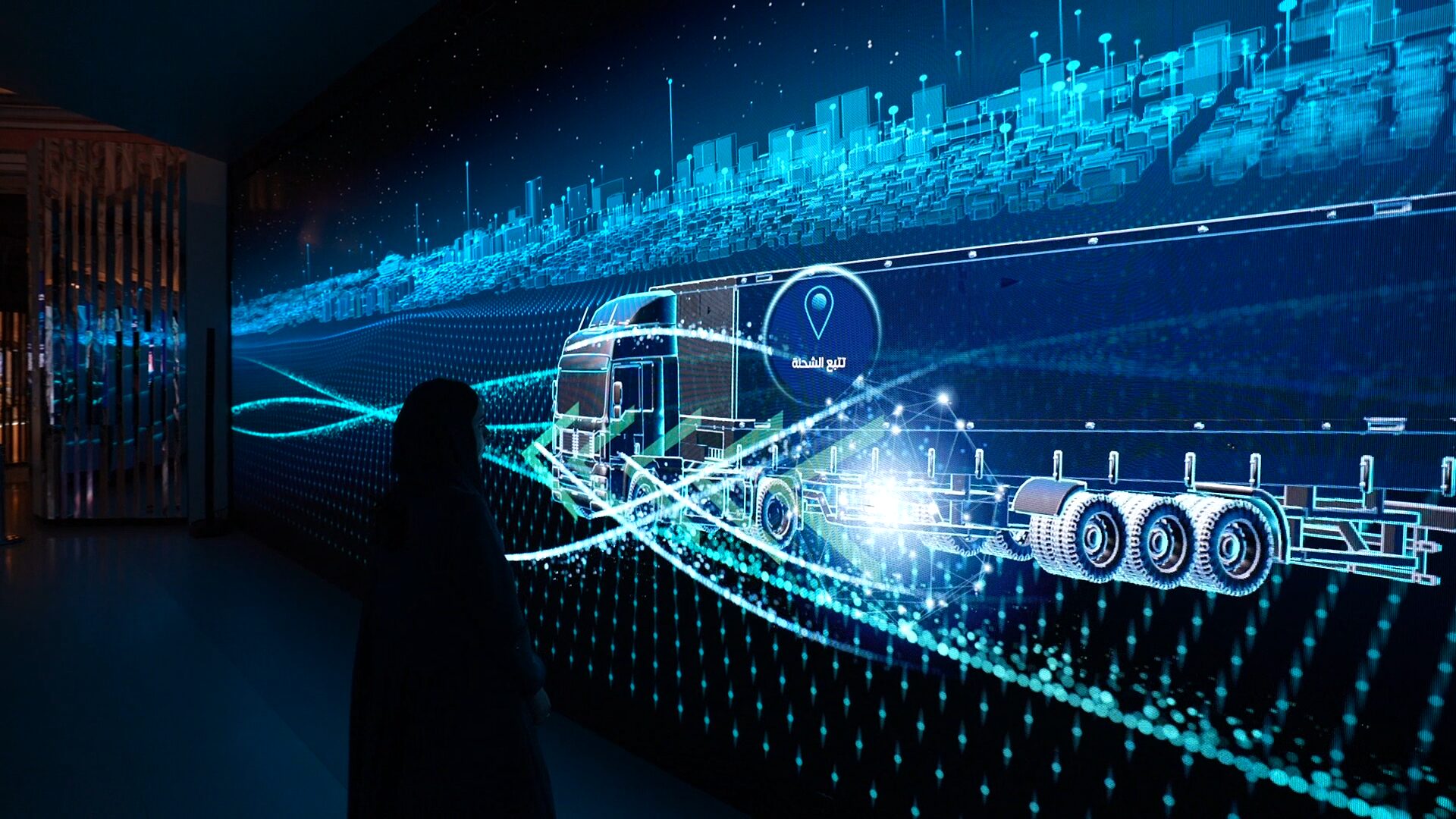 A visitor stands in front of an LED wall showing a glowing truck travelling along blue light trails past a digital skyline.