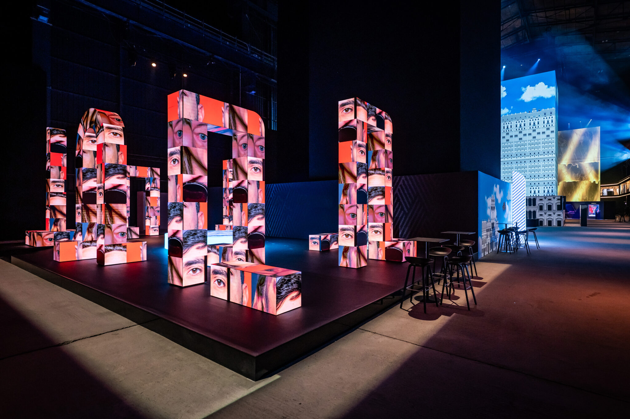 Stage with stacked cubes covered in colourful collage artwork beside a sky-blue display.