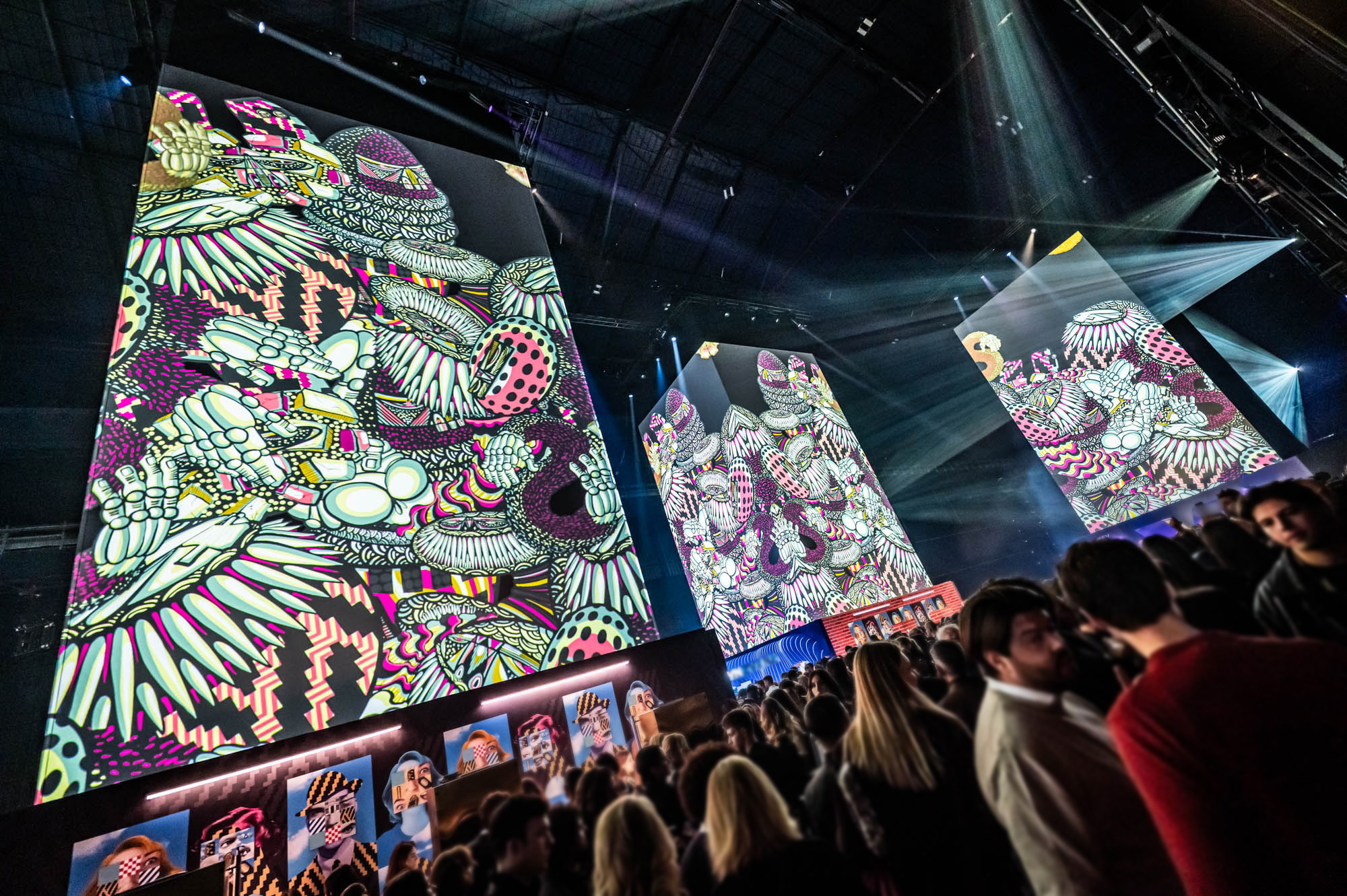 Guests beneath towers projection-mapped with colourful artist illustrations.