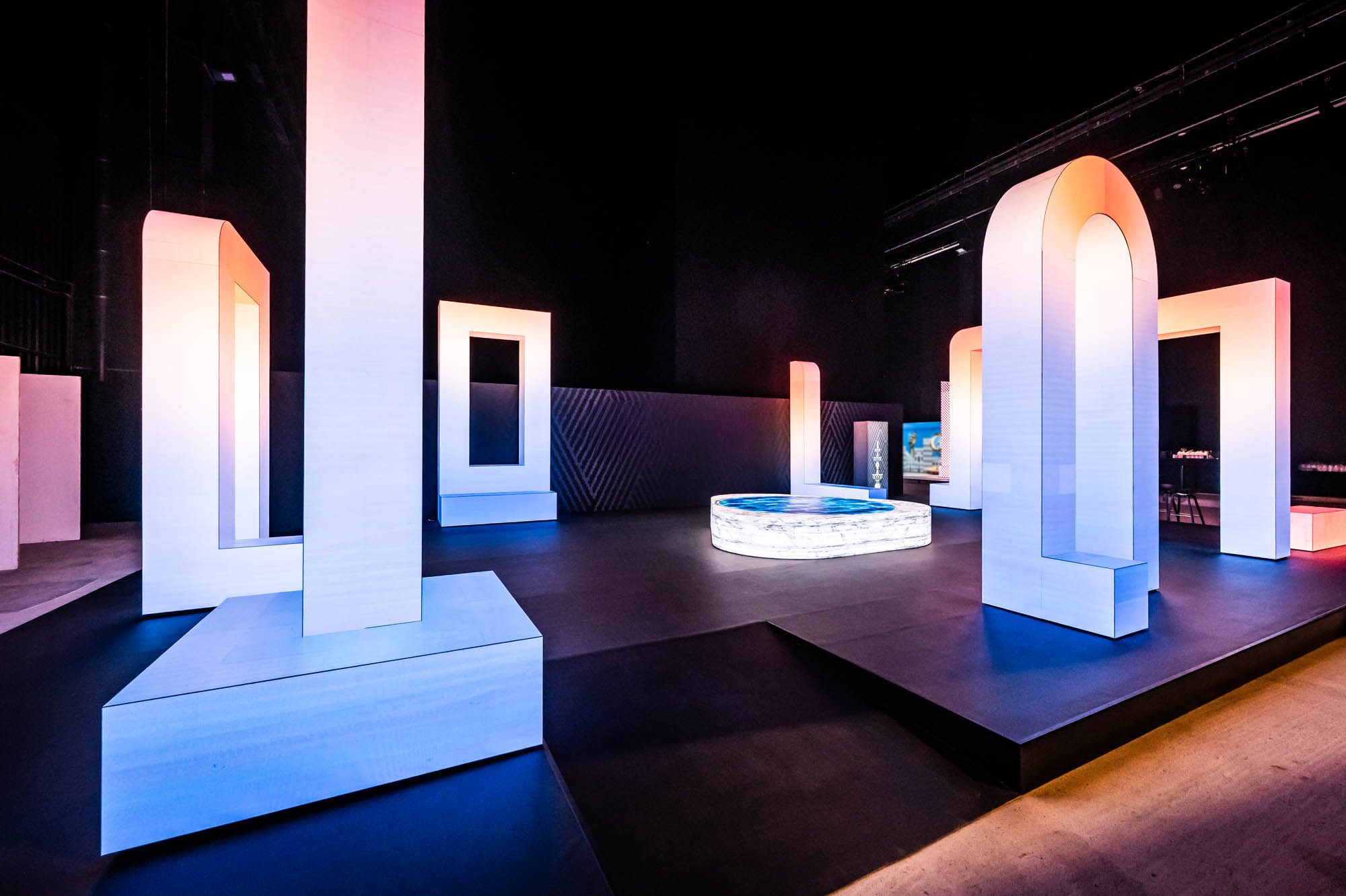 White arch sculptures lit in blue and pink on the empty exhibition floor before doors open.