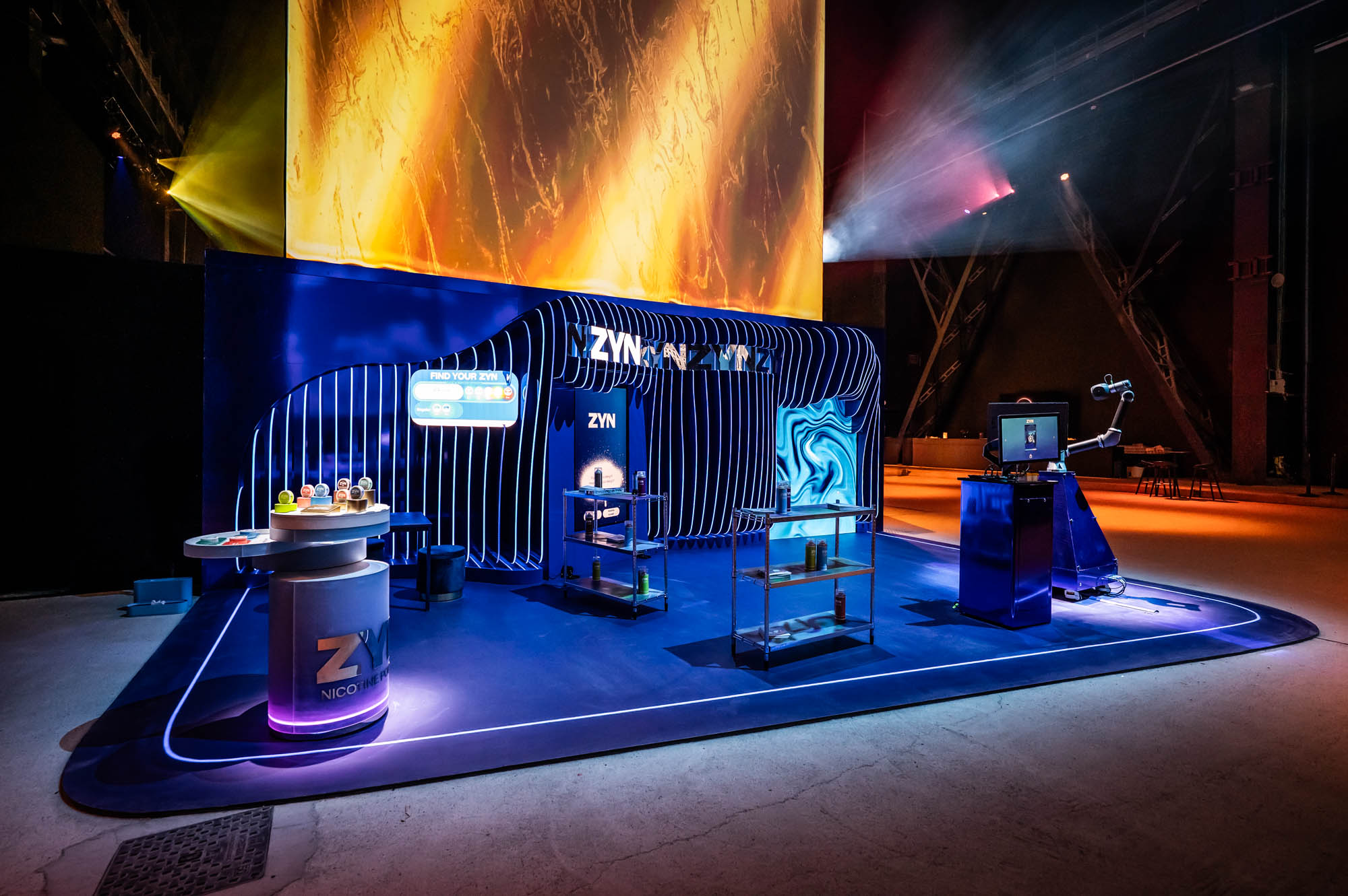 Interactive zone with a robotic arm and swirling digital screens inside a blue-lit ribbed installation.