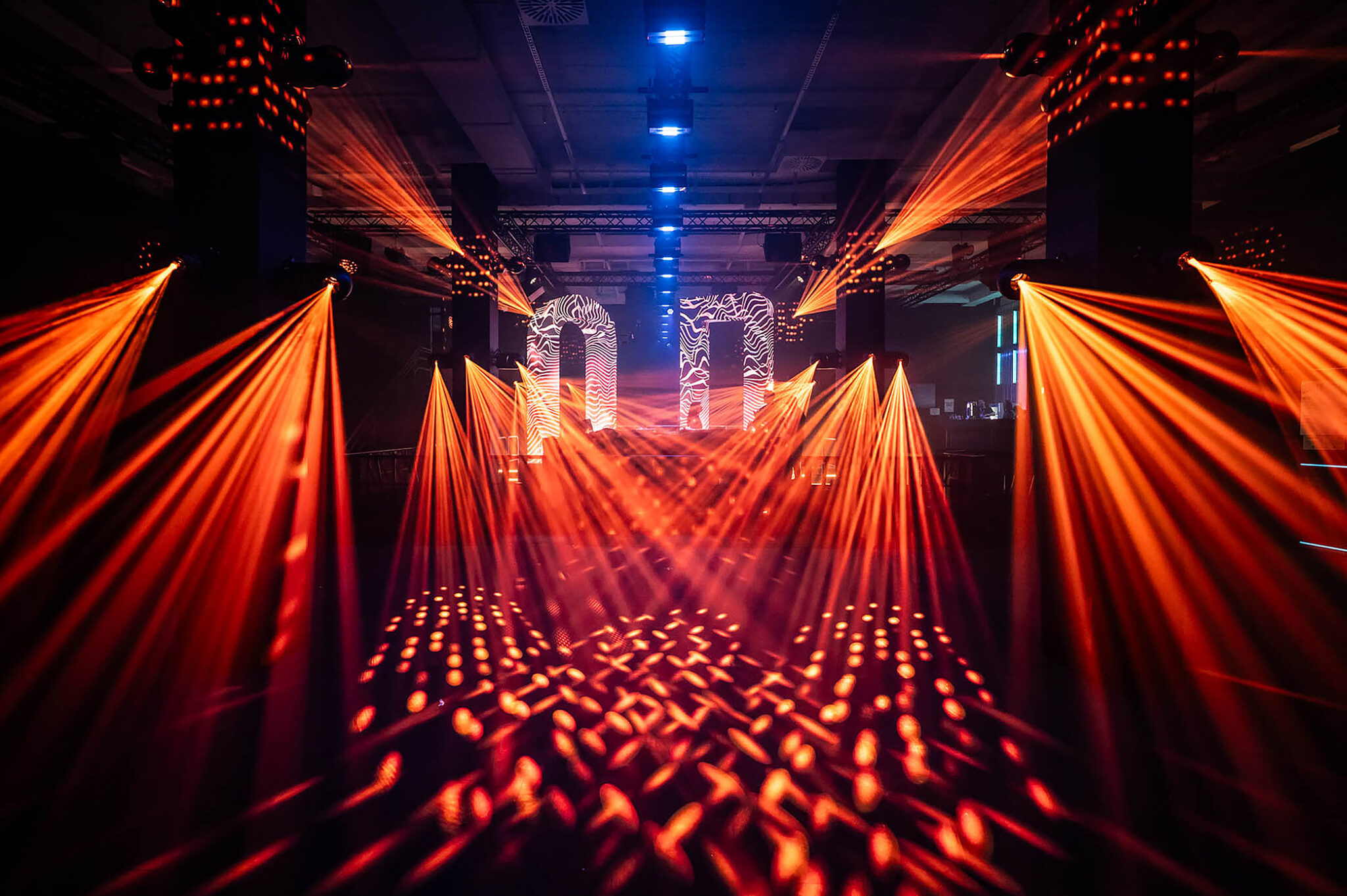Orange beams projecting light patterns onto the dance floor from the ceiling rig.