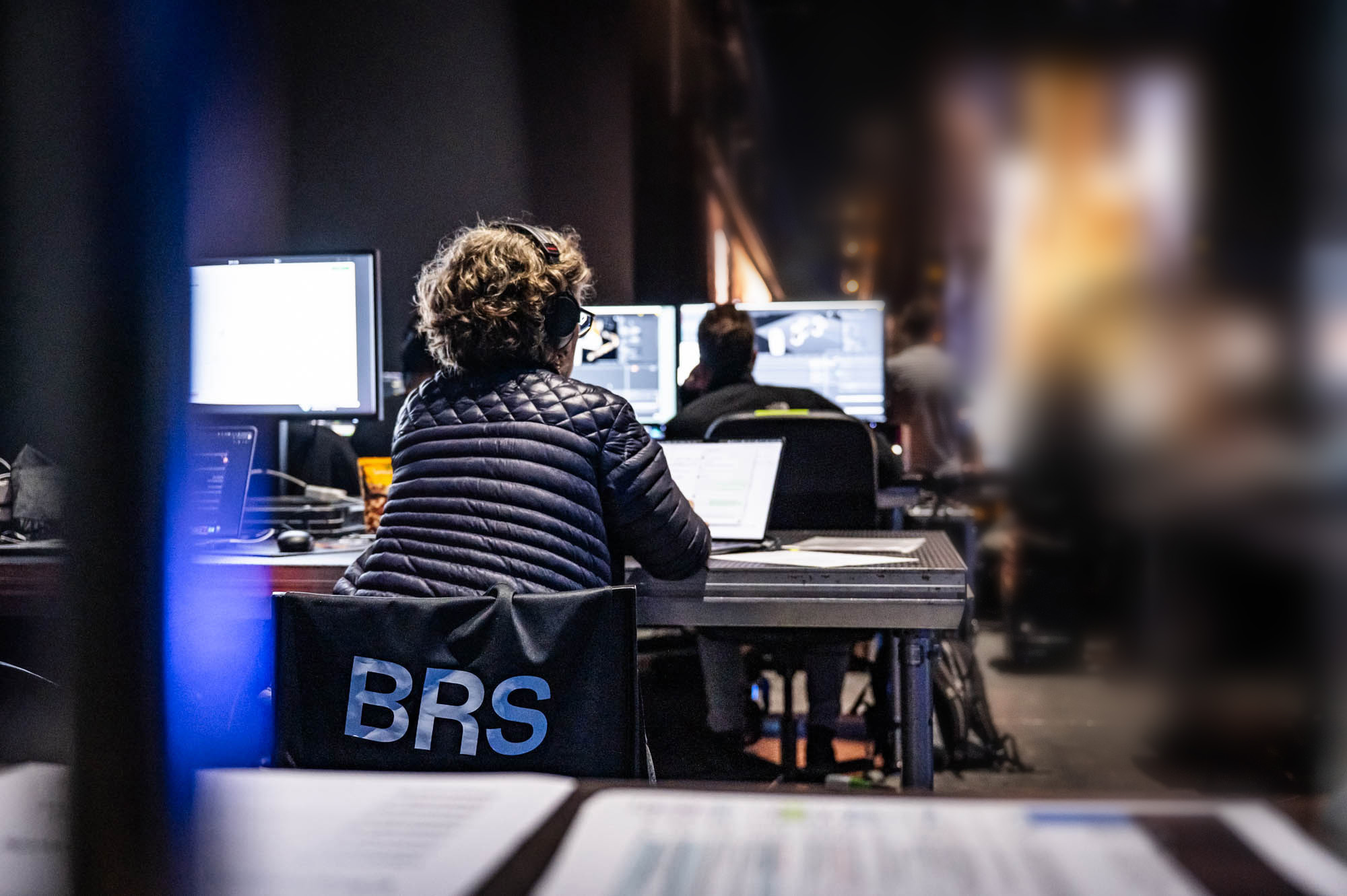 Crew member at a control desk with multiple screens, facing the stage.