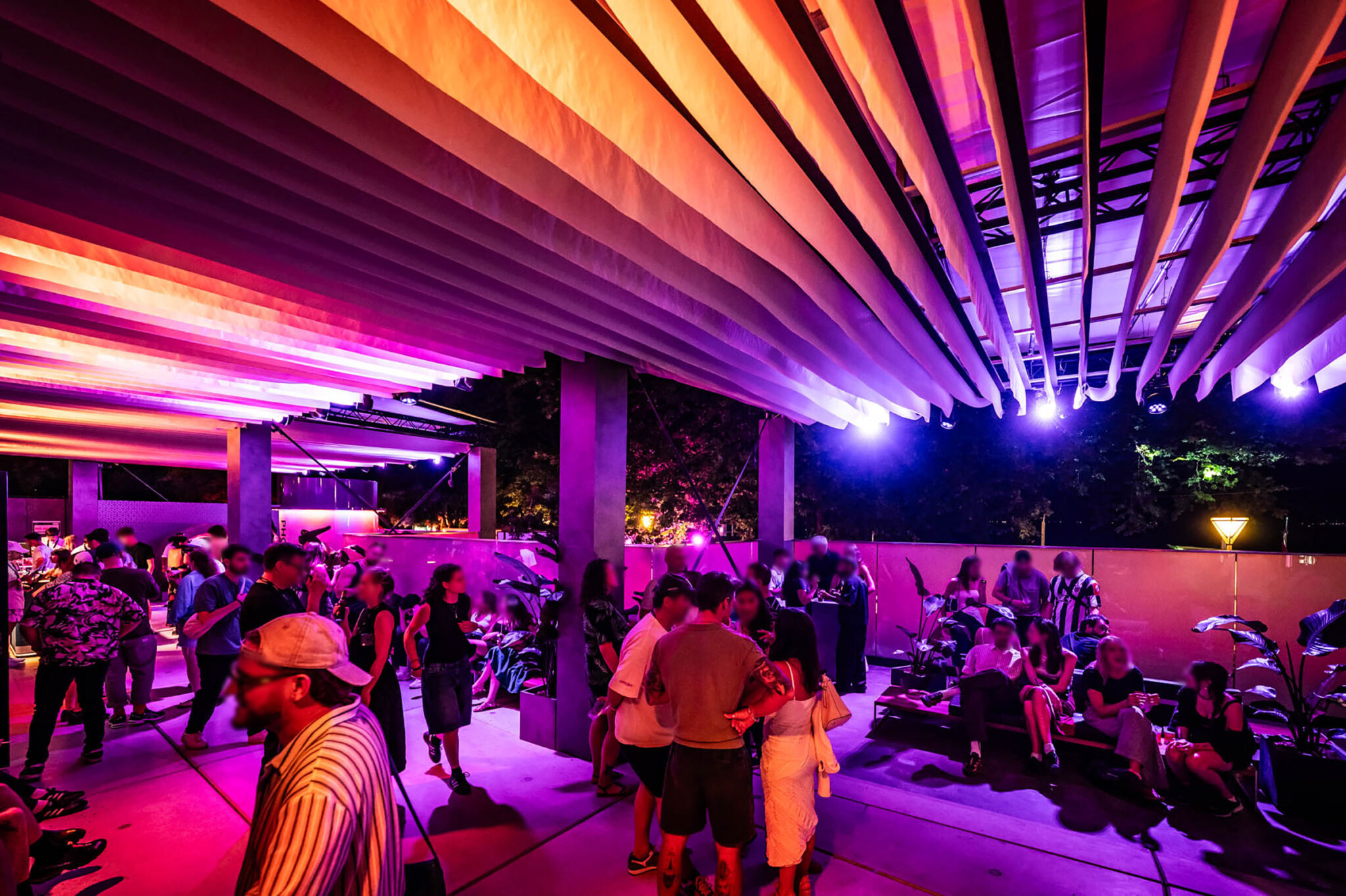Guests gathered on the open-air terrace beneath a canopy lit in orange and violet.