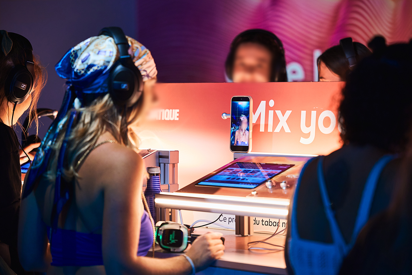 Guests wearing headphones use touchscreen mixing stations in front of a Mix your music sign.