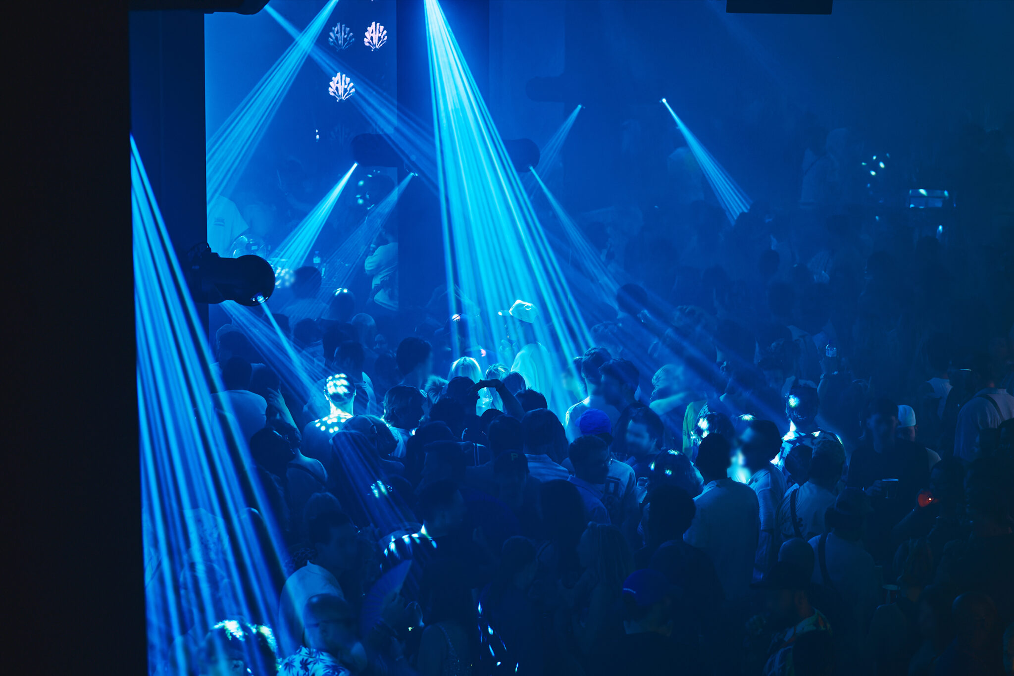 Crowd dancing under blue laser beams on the lower-level dance floor of Club Duplex.