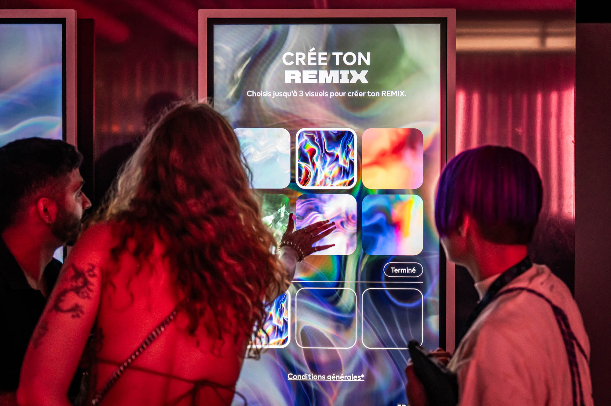 Three guests stand at the Remix Zone touchscreen selecting colourful artwork tiles.