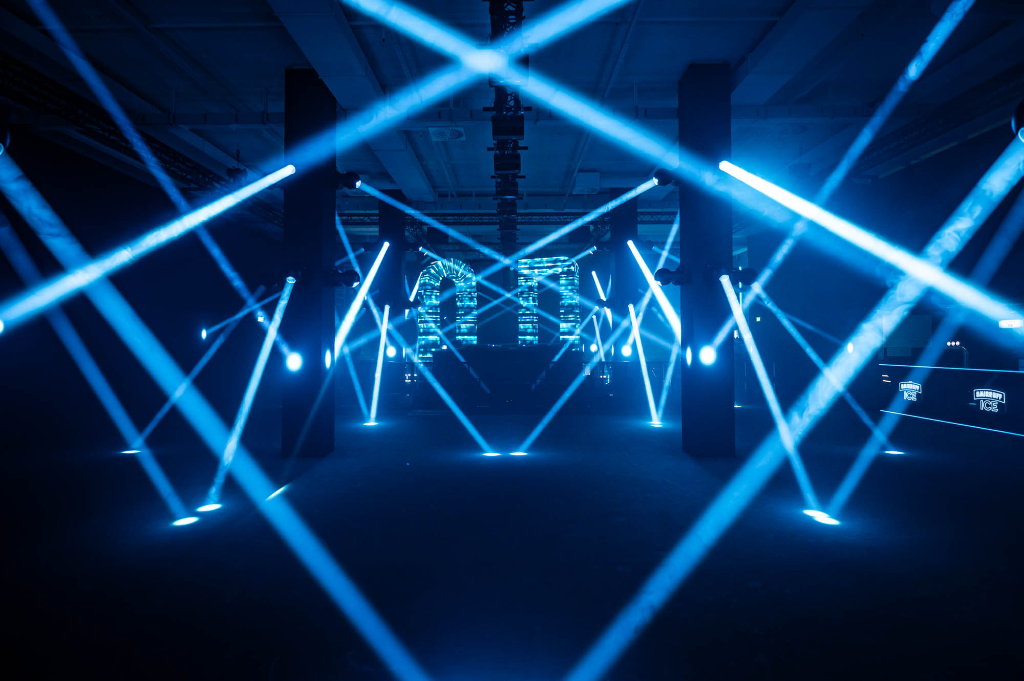 Blue light beams crossing above the empty dance floor between the LED columns.