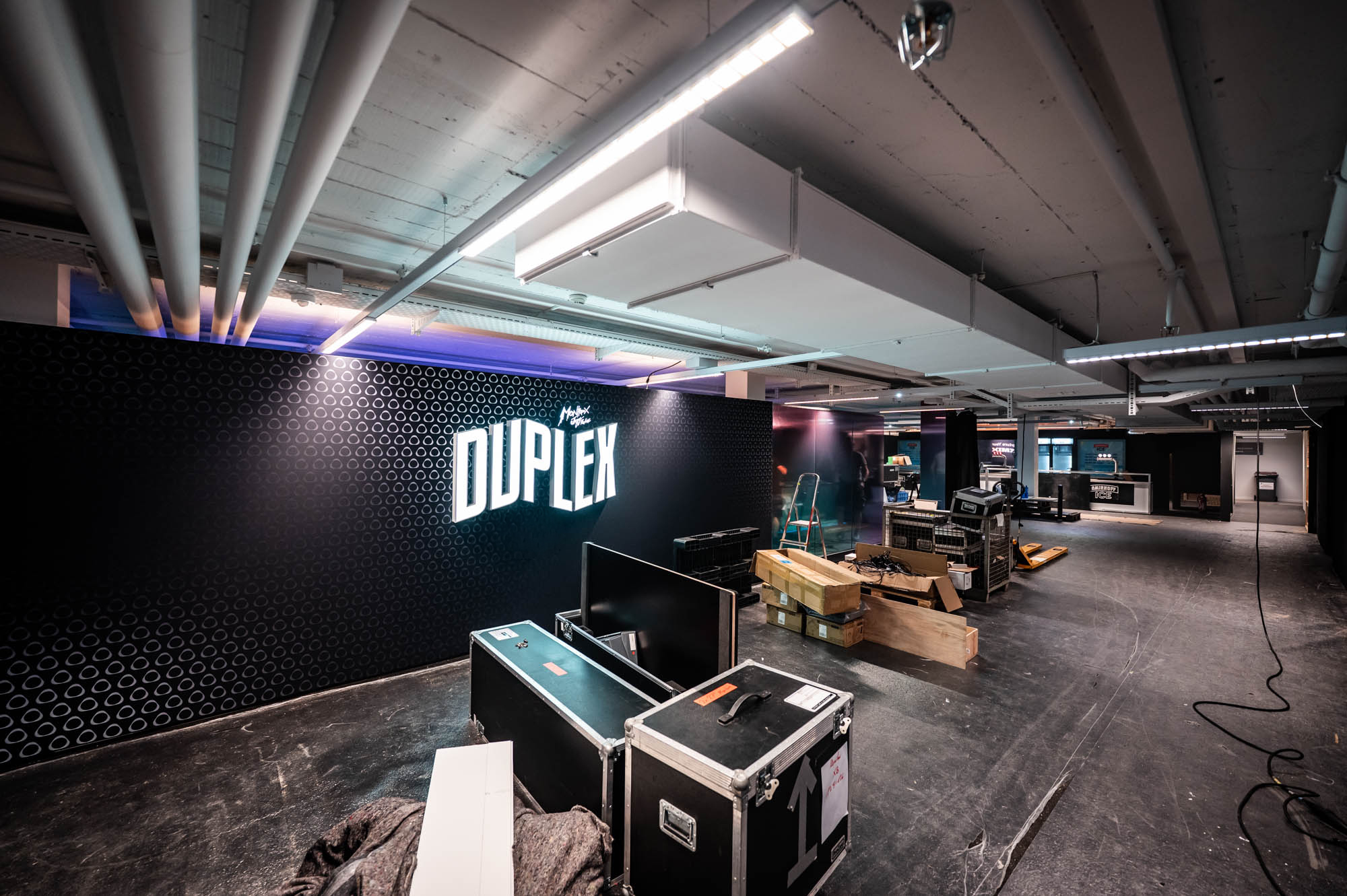 Duplex logo wall during build-up, with flight cases, screens and cables on the floor.